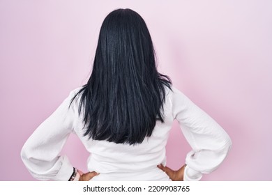 Mature Hispanic Woman Standing Over Pink Background Standing Backwards Looking Away With Arms On Body 