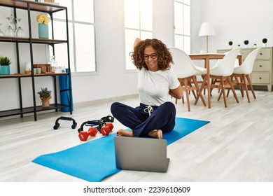 Mature hispanic woman stretching body muscles looking at tutorial video at the living room at home - Powered by Shutterstock