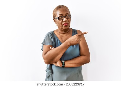 Mature Hispanic Woman Wearing Glasses Standing Over Isolated Background Pointing With Hand Finger To The Side Showing Advertisement, Serious And Calm Face 