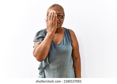 Mature Hispanic Woman Wearing Glasses Standing Over Isolated Background Covering One Eye With Hand, Confident Smile On Face And Surprise Emotion. 