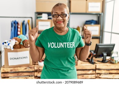 Mature Hispanic Woman Wearing Volunteer T Shirt At Donations Stand Screaming Proud, Celebrating Victory And Success Very Excited With Raised Arms 