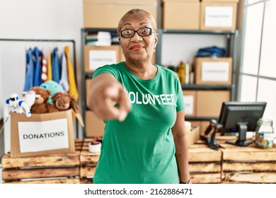 Mature Hispanic Woman Wearing Volunteer T Shirt At Donations Stand Pointing With Finger To The Camera And To You, Confident Gesture Looking Serious 