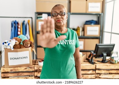 Mature Hispanic Woman Wearing Volunteer T Shirt At Donations Stand With Open Hand Doing Stop Sign With Serious And Confident Expression, Defense Gesture 