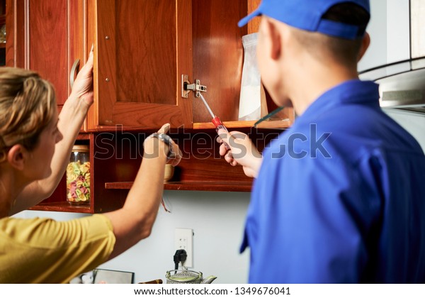 Mature Housewife Showing Repairman Broken Cabinet Stock Photo