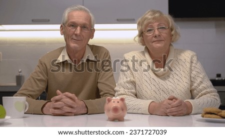 Mature husband and wife looking at the camera with a piggy bank standing on the table, signifying their bank deposit
