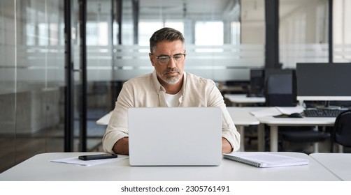 Mature Indian or Latin business man trader using computer, typing, working in modern office, doing online internet research on laptop. Horizontal photo with copy space banner for website header design - Powered by Shutterstock