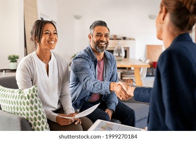 Mature indian man shaking hands with financial advisor at home. Happy smiling couple greeting broker with handshake at home. Multiethnic mid adult man and hispanic woman sealing a contract.