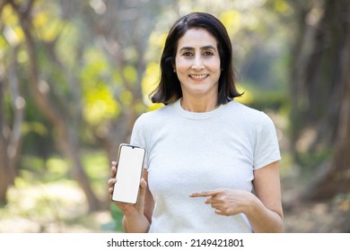 Mature Indian Woman Showing Blank Phone Screen While Standing In The Park Outdoors, Female Displaying Empty Smart Phone For Advertisement And Branding, Online Payment App, Selective Focus.