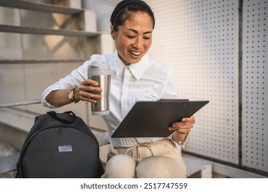 Mature japanese businesswoman sit on staircase and read clipboard while drink coffee - Powered by Shutterstock