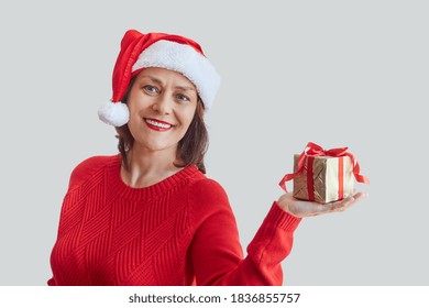 Mature joyful woman in a Santa hat, with New Year's gifts in her hands. Christmas, new year concept. - Powered by Shutterstock