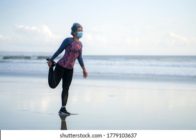 mature lady in face mask stretching before new normal running workout - attractive and happy middle aged woman stretching legs before quarantine beach jogging post quarantine - Powered by Shutterstock