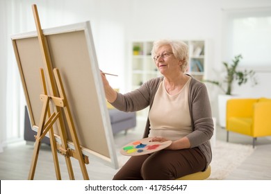 Mature Lady Painting On A Canvas With A Paintbrush At Home