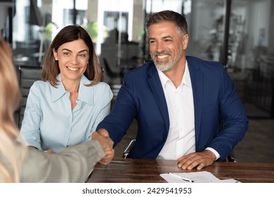 Mature Latin businesspeople of woman and European business man shaking hands with colleagues, partners or employees, signing a contract. Group of people satisfied with results of team work together. - Powered by Shutterstock