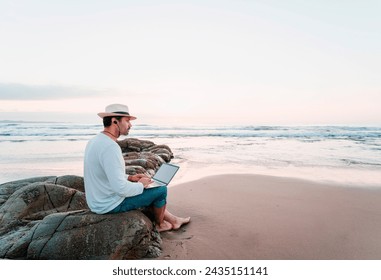 mature latin digital nomad sitting on the beach with a laptop working at sunset over the ocean - Powered by Shutterstock