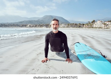 mature latin man surfer stretching on the beach before going in to surf the waves - Powered by Shutterstock