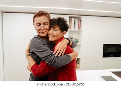 Mature Lesbian Couple Hugging And Smiling In Kitchen At Home