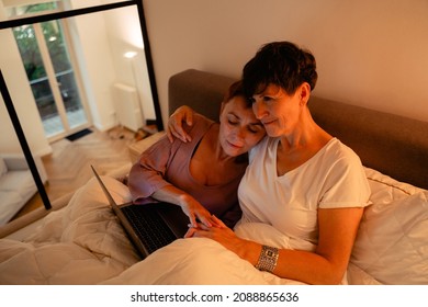 Mature Lesbian Couple Hugging And Using Laptop In Bed At Home