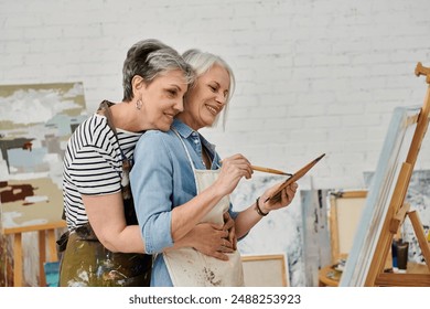 A mature lesbian couple share a loving embrace while painting together in their art studio. - Powered by Shutterstock