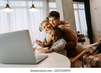 Mature lesbian couple and their adopted son using laptop during breakfast at home - Powered by Shutterstock