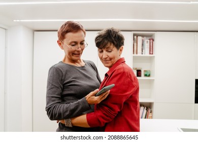 Mature Lesbian Couple Using Cellphone While Hugging At Home