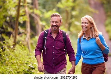 Mature Loving Couple In Countryside Hiking Along Path Through Forest Together Holding Hands - Powered by Shutterstock