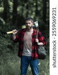 Mature Lumberjack with serious face holds axe in the forest. A lumberjack with an ax examines the tree before felling. Serious lumberjack. Millennial middle aged man holding a big axe outdoor.