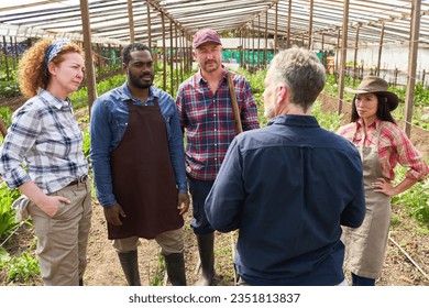 Mature male agronomist discussing with farmers while standing at greenhouse - Powered by Shutterstock