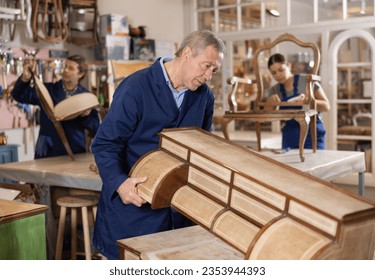 Mature male carpenter working on making vintage commode in workshop