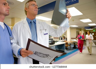 Mature Male Doctor Checking X-ray In Busy Hospital Ward