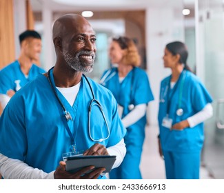 Mature Male Doctor With Digital Tablet In Hospital With Colleagues In Background - Powered by Shutterstock