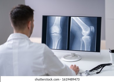 Mature Male Doctor Examining Knee X-ray In Clinic