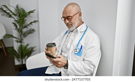 Mature male doctor in glasses using smartphone during break in hospital interior, holding coffee cup. - Powered by Shutterstock