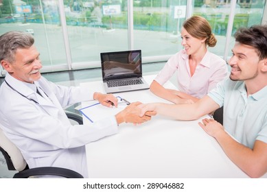 Mature Male Doctor Greeting His New Patients At Clinic.