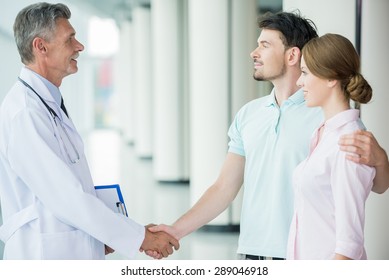 Mature Male Doctor Greeting His New Patients At Clinic.