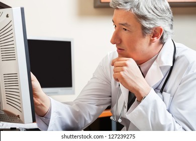 Mature Male Doctor Looking At Computer Screen In Clinic