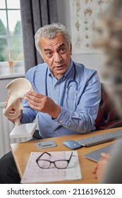 Mature Male Doctor Meeting With Female Patient Discussing Joint Pain In Hip Using Anatomical Model