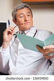 Mature Male Doctor Reading Medical Report Of A Patient