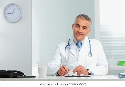 Mature Male Doctor Sitting At Desk In Doctor's Room