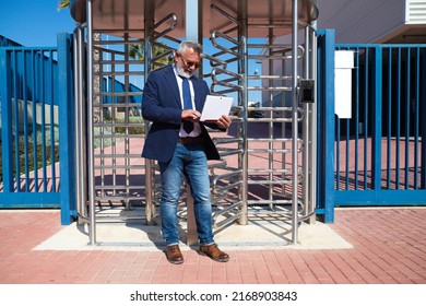 Mature Male Executive, Grey-haired, Bearded, With Sunglasses, Jacket And Tie Is Consulting His Laptop Computer In The Street. Concept Businessman And Executive.