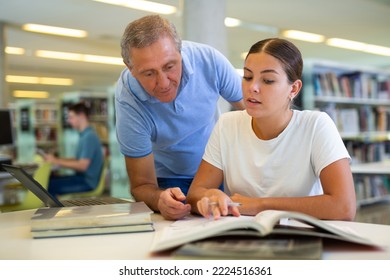 Mature Male Explaining Information For Casual Female While She Is Reading Books In The Library. High Quality Photo