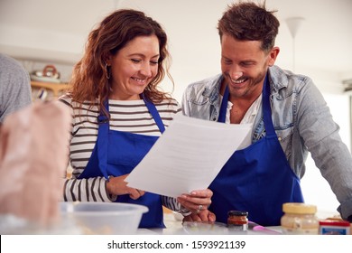 Mature Male And Female Adult Students Looking At Recipe In Cookery Class In Kitchen