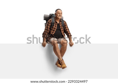 Mature male hiker with a backpack sitting on a blank panel isolated on white background