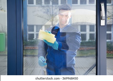 Mature male janitor cleaning glass with rag