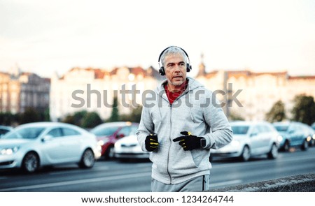 Mature male runner with headphones running outdoors on the bridge in Prague city.