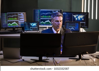 Mature Male Stock Market Broker Looking At Multiple Computer Screen In Office