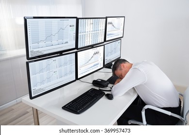 Mature male stock trader sleeping at multiple computer's desk in office