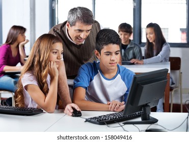 Mature Male Teacher Assisting Teenage School Students In Computer Class