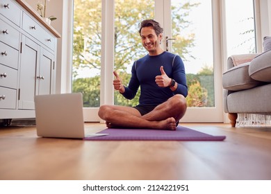 Mature Male Teacher Sitting On Mat At Home With Laptop Giving Online Yoga Class