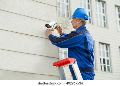 Mature Male Technician Installing Camera On Wall With Screwdriver