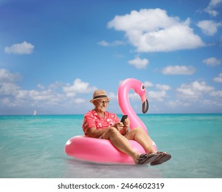 Mature male tourist sitting on a famingo swimming ring in the sea and using a smartphone - Powered by Shutterstock